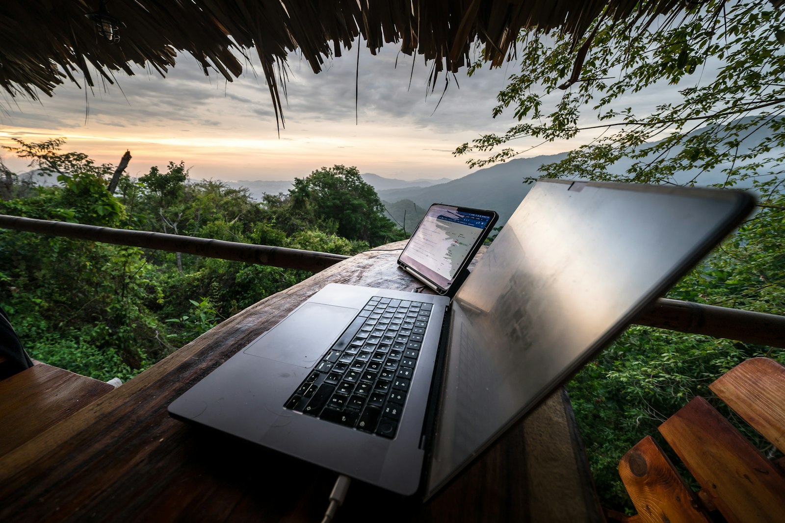 A laptop open on a wooden table with a mountain view in the background